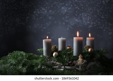 Third advent with three burning candles on fir branches with Christmas decoration against a dark grey background, copy space, selected focus, narrow depth of field
