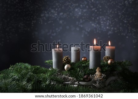 Third advent with three burning candles on fir branches with Christmas decoration against a dark grey background, copy space, selected focus, narrow depth of field