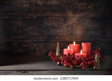 Third advent wreath with red candles, three are lit, decoration with berries, Christmas balls and small wooden trees, dark rustic background, copy space, selected focus, narrow depth of field