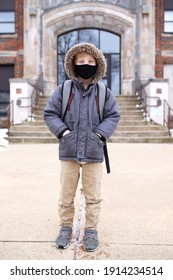 A Third Grade Boy Child Wearing A Protective Covid Face Mask Is Smiling Happily As He Stands Outside His Elementary School Education Building During The Pandemic.