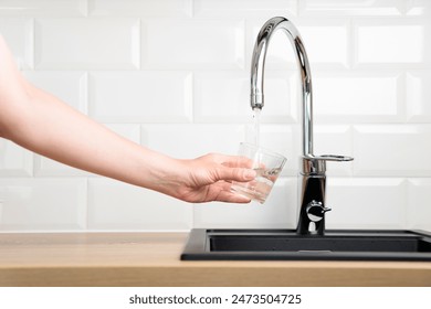 Thirst human wanted to drink water and filling up a glass of tap pure water from kitchen faucet with white tiles wall. Concept of purity and cleanness of natural water with copy space