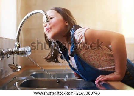 The thirst is real. Shot of a little girl drinking water directly from the kitchen tap at home.