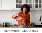 Thirsty Black Woman Pouring Water From Jug To Glass In Kitchen Interior, Portrait Of Happy Smiling African American Female Drinking Healthy Liquid At Home, Enjoying Refreshing Drink, Copy Space