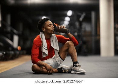 Thirsty exhausted sweaty diverse sportsman sitting on a gym floor and drinking water. - Powered by Shutterstock