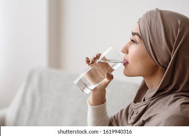 Thirsty islamic woman in headscarf drinking mineral water from glass at home, selective focus, empty space - Powered by Shutterstock