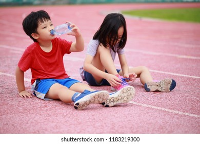 Thirsty little asian boy and girl drinking water and rest at the school athletic field.