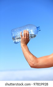 Thirsty Man Drinking Water Of Big Bottle. Closeup Of Hand Holding Bottle. Thirst Concept Image From Outdoors On Blue Sky Above The Clouds.