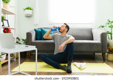 Thirsty Man In His 30s Taking A Break And Drinking Water From A Bottle After Doing A Home Workout In The Living Room 