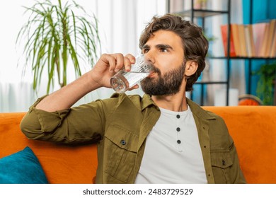 Thirsty man hold glass of natural filtered aqua make sips drinking still water preventing dehydration at home room. Water after reverse osmosis filter. Guy with good life habits, healthy, weight loss - Powered by Shutterstock