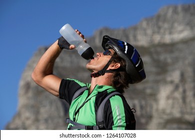 Thirsty man on mountain bike drinking water from bottle on active vacation in profile