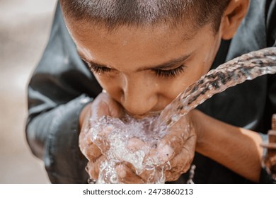 A thirsty Pakistani boy drinking water from a water supply tap on a hot day - Powered by Shutterstock