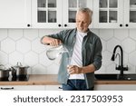 Thirsty Senior Man Pouring Water From Jug To Glass In Kitchen Interior, Portrait Of Happy Smiling Elderly Gentleman Drinking Healthy Liquid At Home, Enjoying Refreshing Drink, Copy Space