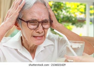 Thirsty Senior Woman With A Brain Freeze After Drinking Cold Water With Ice,Asian Old Elderly Touching Her Head With Hands,pain In Head Induced By The Consumption Of Very Cold Drink,drink It Too Fast