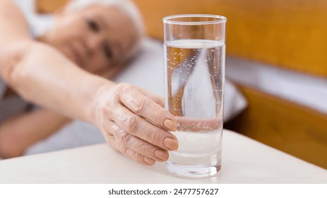 Thirsty senior woman taking glass of water lying in bed, start new day with fresh aqua, panorama - Powered by Shutterstock