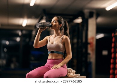 A thirsty and tired sportswoman is taking a break and drinking water in a gym. - Powered by Shutterstock