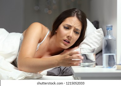 Thirsty woman reaching a glass of water lying on the bed in the night at home