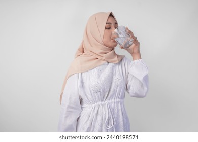 Thirsty young Asian Muslim woman in white dress and cream veil hijab drinking fresh mineral water after fasting. Ramadan concept - Powered by Shutterstock