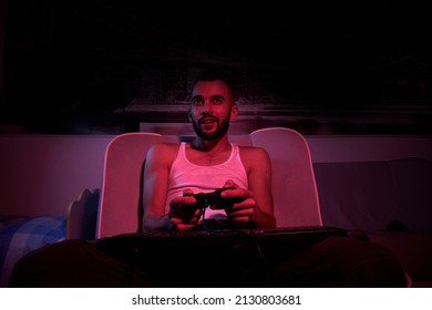 A Thirty-year-old Guy With A Joystick In His Hands Is Playing Computer Games, Experiencing Various Emotions. Sitting On The Couch At Home. View From The TV Side.