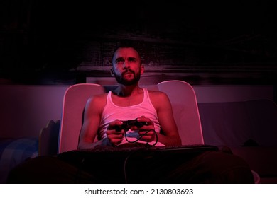 A Thirty-year-old Guy With A Joystick In His Hands Is Playing Computer Games, Experiencing Various Emotions. Sitting On The Couch At Home. View From The TV Side.