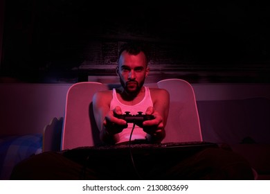 A Thirty-year-old Guy With A Joystick In His Hands Is Playing Computer Games, Experiencing Various Emotions. Sitting On The Couch At Home. View From The TV Side.