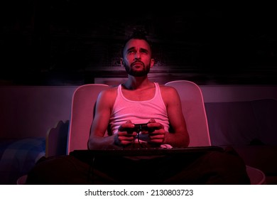 A Thirty-year-old Guy With A Joystick In His Hands Is Playing Computer Games, Experiencing Various Emotions. Sitting On The Couch At Home. View From The TV Side.