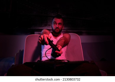 A Thirty-year-old Guy With A Joystick In His Hands Is Playing Computer Games, Experiencing Various Emotions. Sitting On The Couch At Home. View From The TV Side.