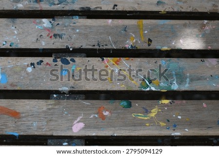 This abstract background features a textured wooden surface covered in vibrant, dried paint splatters and drips, suggesting artistic activity and creative expression