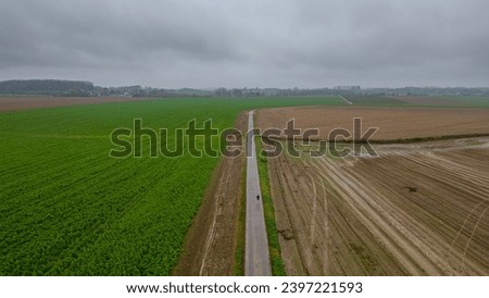 This aerial image presents a striking juxtaposition of agricultural land use, where a vibrant green field of young crops contrasts sharply with the adjacent bare brown soil of a recently harvested or