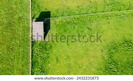 This aerial photograph captures a solitary small shed with a gabled roof in the middle of a vibrant green pasture. The structure casts a crisp shadow on the ground, indicating the sun is at its zenith Сток-фото © 
