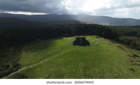 This aerial shot captures the Hellfire Club’s brooding ruins atop Montpelier Hill on a warm day. Sunlight bathes its crumbling stone walls, contrasting with the lush Dublin Mountains. Shadows stretch 