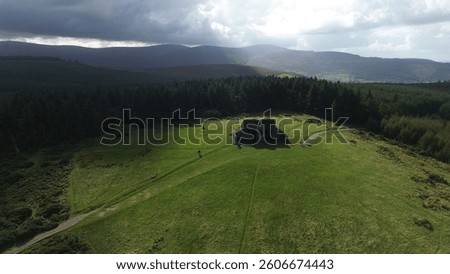 This aerial shot captures the Hellfire Club’s brooding ruins atop Montpelier Hill on a warm day. Sunlight bathes its crumbling stone walls, contrasting with the lush Dublin Mountains. Shadows stretch 