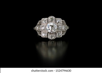 This antique diamond engagement ring with a one plus carat center stone is surrounded by accent side diamonds and set in platinum. Shown on a black reflective background.
Keywords