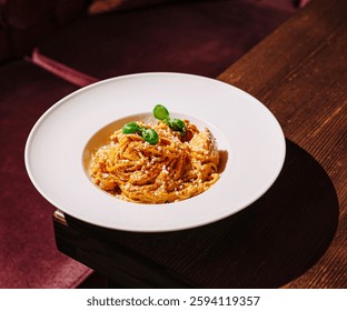 This appetizing dish features strands of spaghetti mixed with a savory sauce, garnished with fresh basil leaves. The meal is elegantly presented on a white plate in an upscale restaurant.