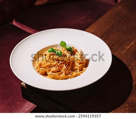 This appetizing dish features strands of spaghetti mixed with a savory sauce, garnished with fresh basil leaves. The meal is elegantly presented on a white plate in an upscale restaurant.