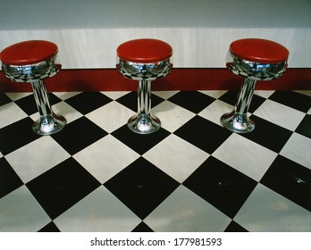 This is an art deco style restaurant. It has a black and white checkerboard tile floor with red vinyl stools next to the counter. It is a typical 50's style diner.