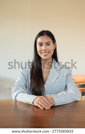 This authentic vertical portrait captures a beautiful young Thai woman from the Isan region looking directly at the camera with a joyful, toothy smile. This genuine and honest representation of a modern Southeast Asian professional showcases a stunning female in a moment of happy, confident engagement. Dressed in a stunning light grey linen blazer with a visible natural texture, she sits at a minimalist wooden table within a bright, airy cafe interior. The stunning subject is captured in a classic headshot style, her cheerful expression and direct eye contact reflecting a real, unretouched human connection. This high-quality lifestyle photograph emphasizes an unaltered aesthetic, ideal for commercial projects seeking authentic representation of professional life, positive work culture, and approachable leadership. The background is a clean, contemporary space featuring a minimalist wall and warm, natural daylight that highlights her genuine features and smooth dark hair. This genuine moment reflects the rising demand for diverse representation in the global workforce, blending elegance with a relaxed, urban atmosphere. The vertical composition is expertly balanced, offering significant negative space and copy space above her for editorial headlines or advertising overlays. Every detail, from the subtle weave of the linen fabric to her friendly, approachable gaze, is rendered with professional clarity. This real-life scenario is perfect for marketing campaigns focused on entrepreneurship, university student life, or modern corporate recruitment. The honest happiness and unretouched skin texture provide a relatable feel that converts exceptionally well in today's visual market. As example of an Esan female, this image serves as a powerful asset for global brands prioritizing inclusion and authentic storytelling. Every pixel of this scene, from the minimalist room to the genuine smile, is designed to resonate with humans searching for honest, high-intent visual content.