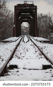 This beautiful image captures a train track running through a snowy, wooded area with an old bridge above it