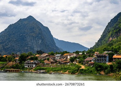 This beautiful image features a body of water next to a lush green hillside filled with towering mountains in the background