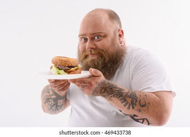 This is the best food ever. Cheerful fat man is holding plate of burger. He is standing and looking at camera with happiness. Isolated