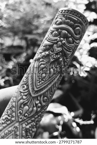 This black and white image features highly detailed ornamental carvings, which appear to be an intricate example of traditional Balinese or Javanese art. The image shows a cylindrical object, potentially a handle of a traditional weapon (like a keris), a decorative pillar, or a part of a musical instrument such as a saput kendang.