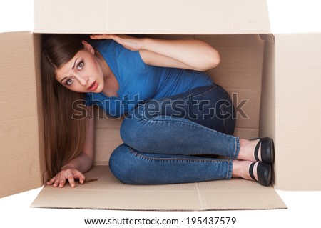 This box is too small. Shocked young woman looking at camera while sitting in a cardboard box