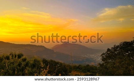 This breathtaking image captures a mesmerizing sunset over a mountain landscape. The sky is painted with a gradient of warm hues, transitioning from a deep golden yellow near the horizon to a soft ora