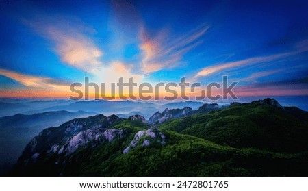 This breathtaking image captures the stunning beauty of a mountainous landscape at sunset. The sky is painted with vibrant colors ranging from deep blues to fiery oranges.
