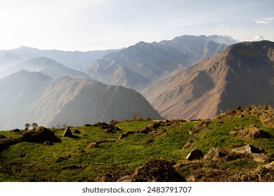 This breathtaking photograph features a lush green hillside bathed in sunlight, overlooking the misty mountain valleys of the Himalayas. The contrast between the vibrant green grass and the layered, m - Powered by Shutterstock