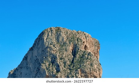 This breathtaking shot captures a steep rock face towering above a crystalclear sea beneath a vibrant blue sky