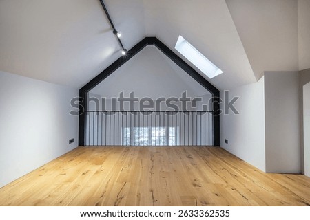This bright loft features a spacious wooden floor, tall walls, and a prominent skylight allowing natural light to illuminate the space. Ideal for creative projects or relaxation.