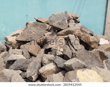 This building material, known as river rock or split stone, is commonly used for house foundations. The pile of stones consists of irregularly shaped pieces of natural stone of various sizes. This material is often sold by volume, such as per cubic meter or per truckload.