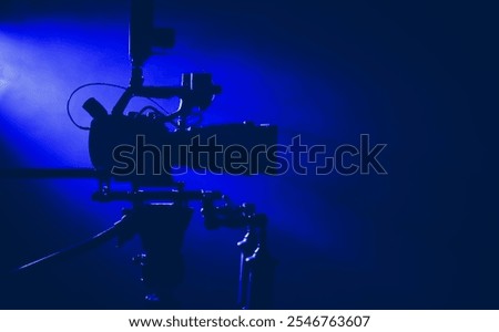 This camera is positioned on a tripod in a dark studio, illuminated by vibrant blue lights, preparing for a film or video production.