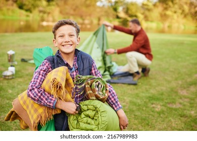 This camping trip is going to be awesome. Portrait of a young boy holding camping gear with his father in the background.