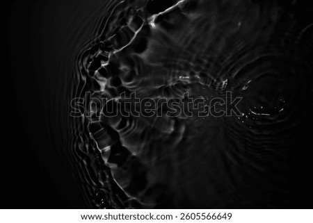 This captivating abstract image showcases the elegant patterns of black water with soft light reflections and ripples, creating a tranquil atmosphere.